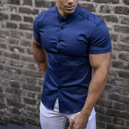 Navy blue short sleeve shirt with dark buttons, worn tucked into white trousers in front of a brick wall. 3