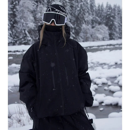Model in the black version of the oversized hooded jacket, hands in pockets, beside a snowy river. 2