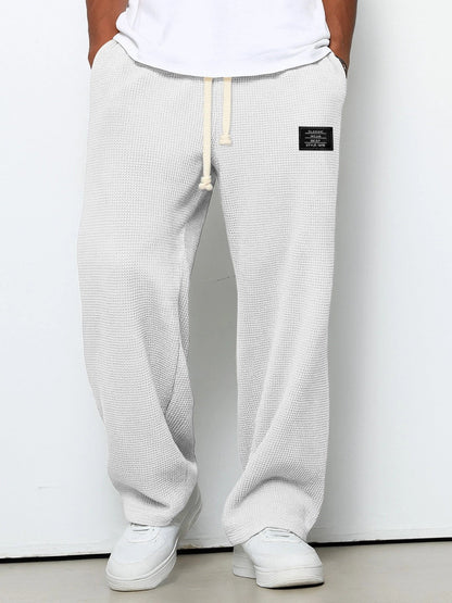 Front view on a model of the trousers in off-white with a pale grey cast, cream drawstring at the waist, worn with white trainers. 2