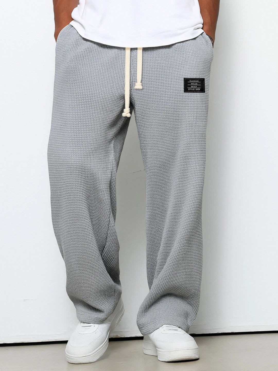 Front view on a model of the trousers in light grey, showing the waffle texture, drawstring waist and small black patch on the hip. 3