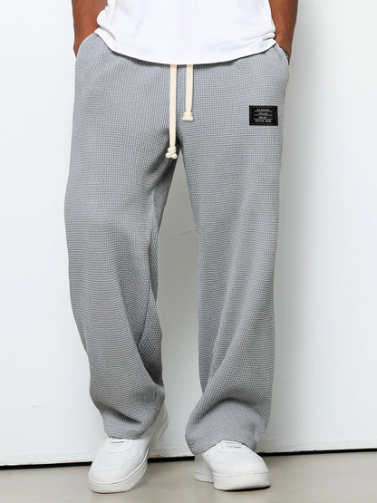 Front view on a model of the trousers in light grey, showing the waffle texture, drawstring waist and small black patch on the hip. 3