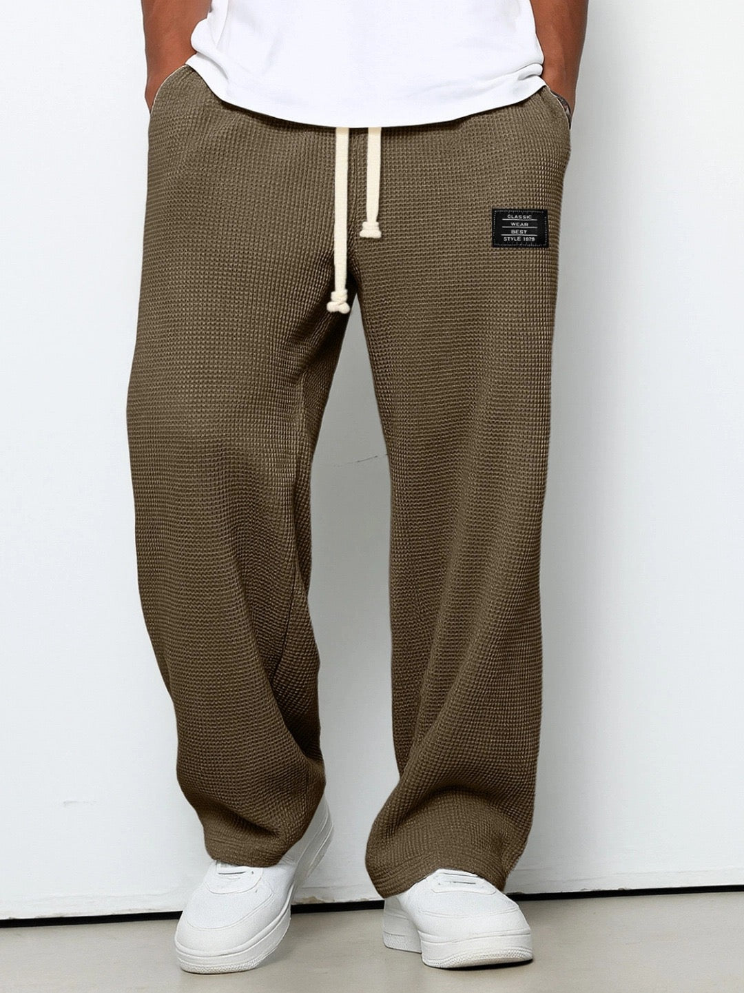 Front view on a model of the trousers in olive brown, with the waffle knit texture, cream drawstring and wide straight legs. 5