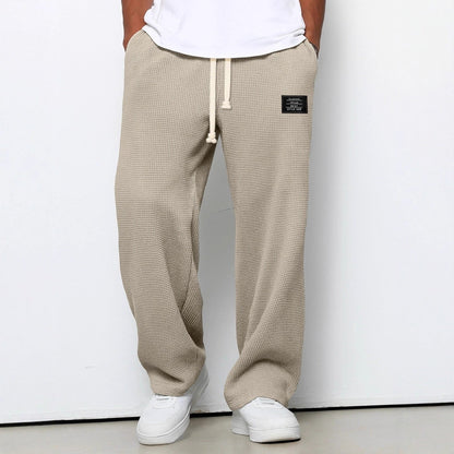 Slightly closer front view of the trousers in beige on a model, showing the cream drawstring, hip patch and relaxed wide legs. 6