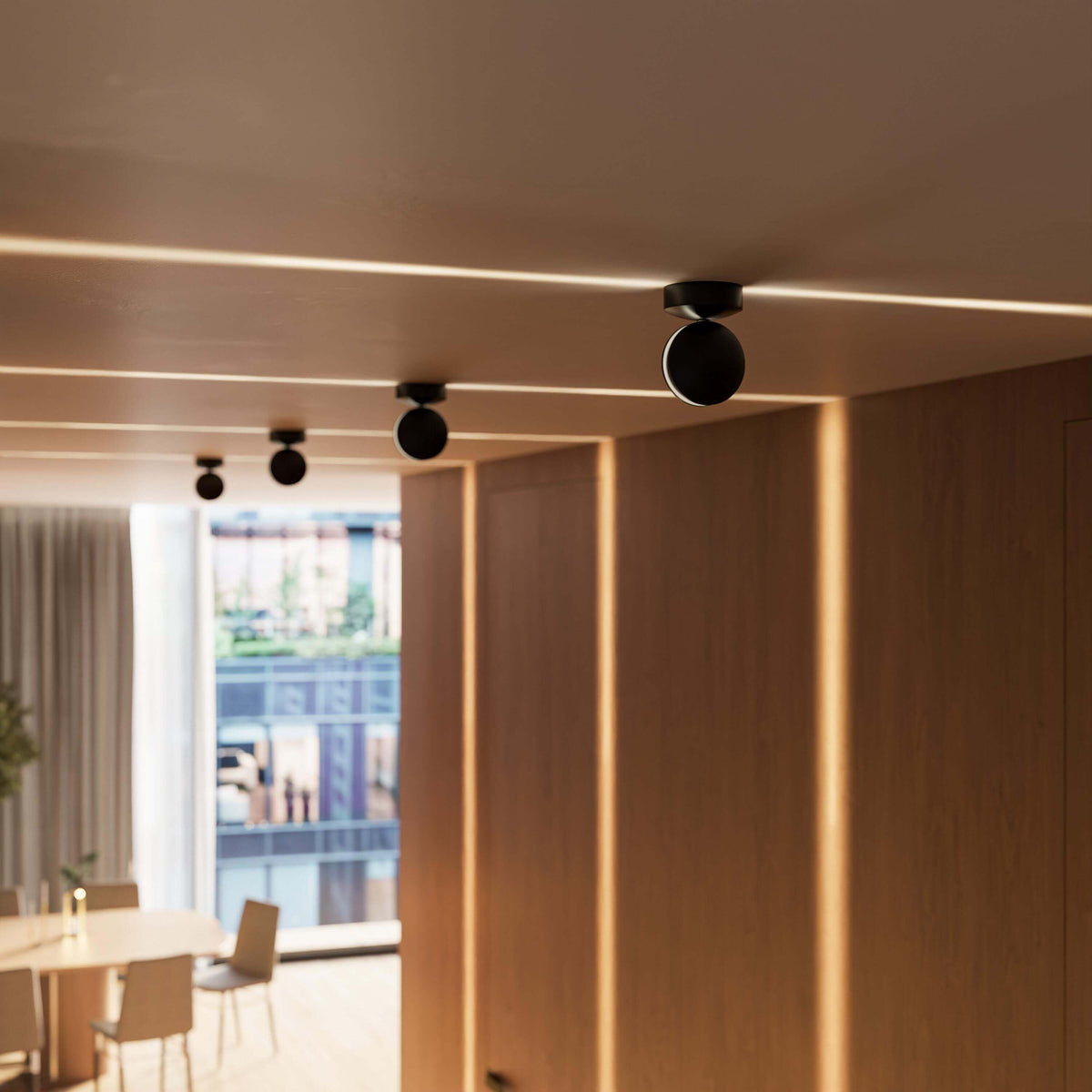 Row of black ceiling lights in a wood-panelled hallway, each casting a warm horizontal line of light, with a dining area beyond. 12