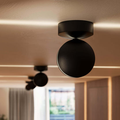 Close view of a black ceiling light with a round head, with a second light blurred behind and warm light lines on the ceiling. 11
