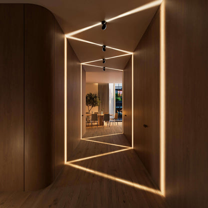 Black ceiling lights in a wood-panelled corridor casting zigzag beams of warm light across the ceiling, walls and floor. 10