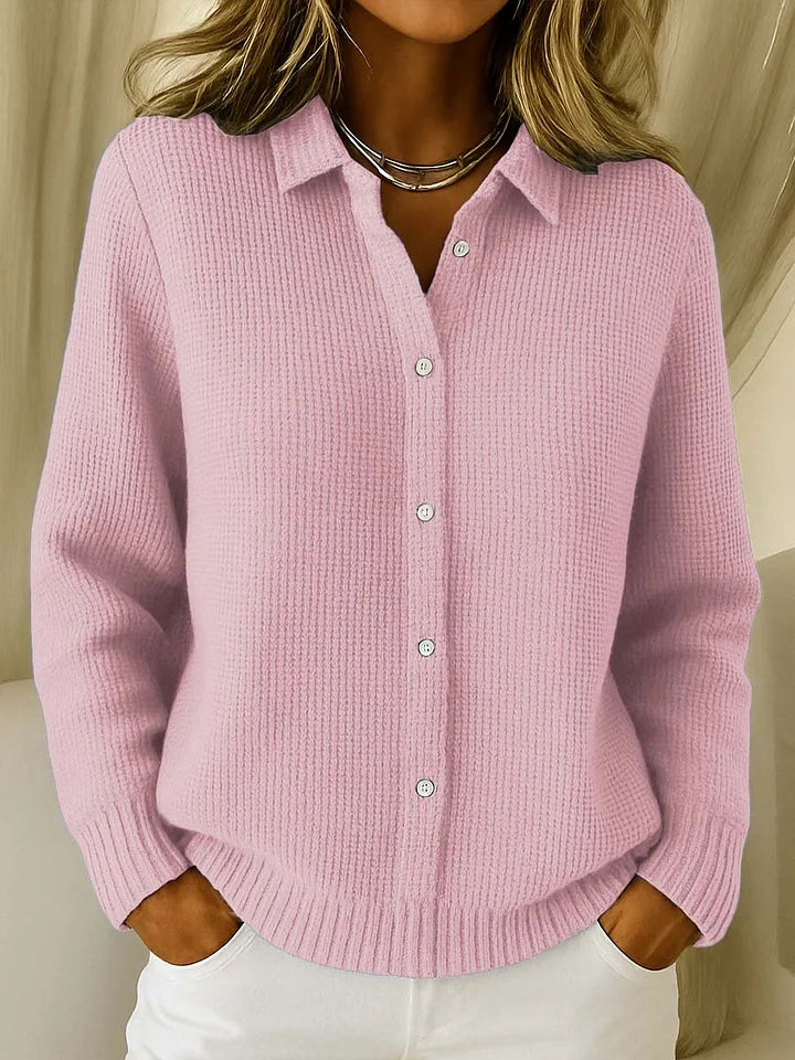 Same buttoned collared jumper in soft pink, worn with white trousers and a silver necklace, hands tucked into pockets. 2