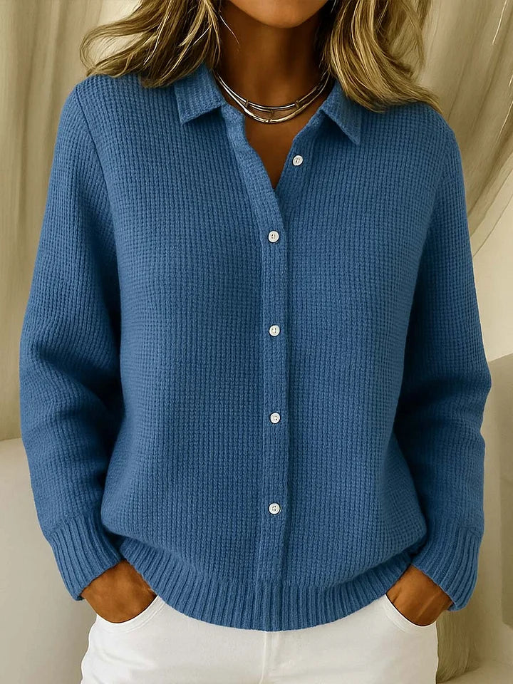 Collared button-up knit jumper in a medium denim blue, worn by a model with white trousers and a layered silver necklace. 4