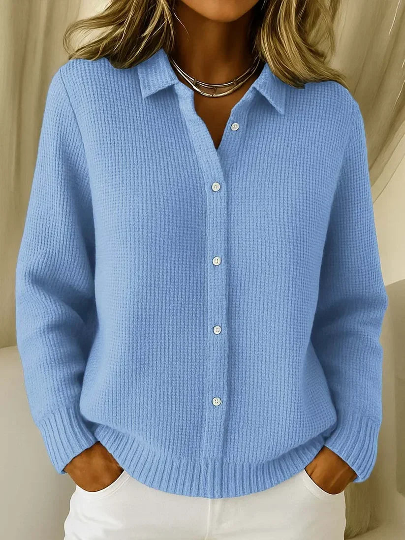 Model wearing the waffle-knit collared jumper in light blue, buttoned down the front, with ribbed cuffs and hem, hands in pockets. 1