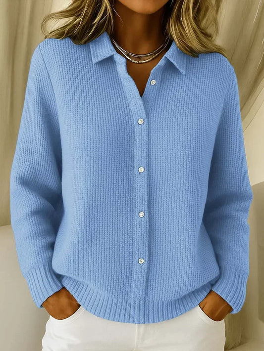 Model wearing the waffle-knit collared jumper in light blue, buttoned down the front, with ribbed cuffs and hem, hands in pockets. 1