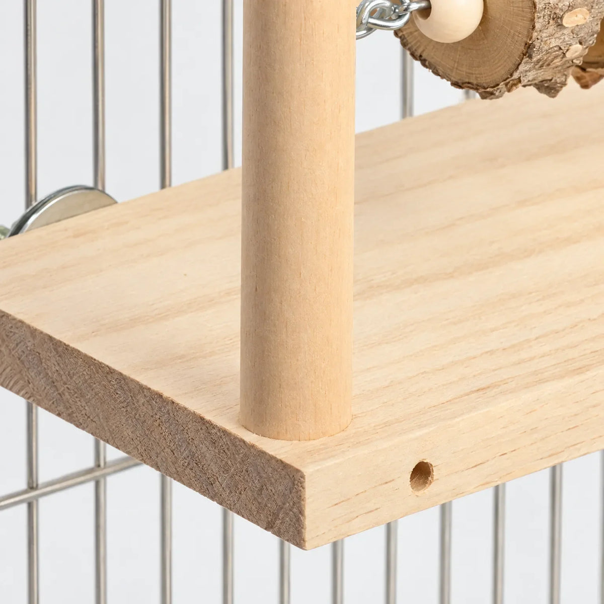 Close-up of the platform's pale wood grain, upright post, drilled hole and metal disc fixing against cage bars. 3