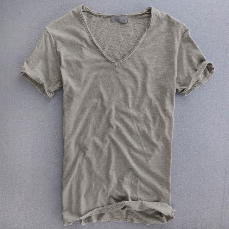 Short-sleeved V-neck t-shirt in light grey laid flat on a grey surface, showing the slubbed texture and rolled sleeve cuffs. 1