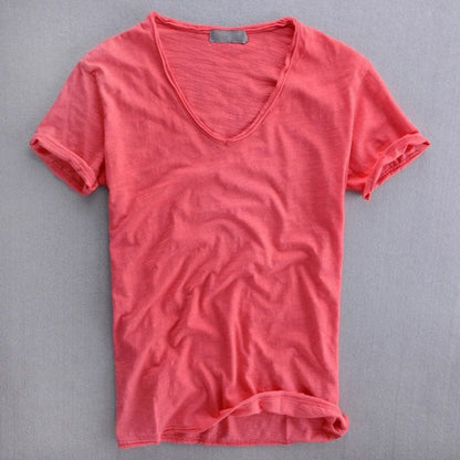 Coral-pink version of the V-neck t-shirt laid flat, showing the textured fabric, small label at the back neck and rolled sleeves. 3