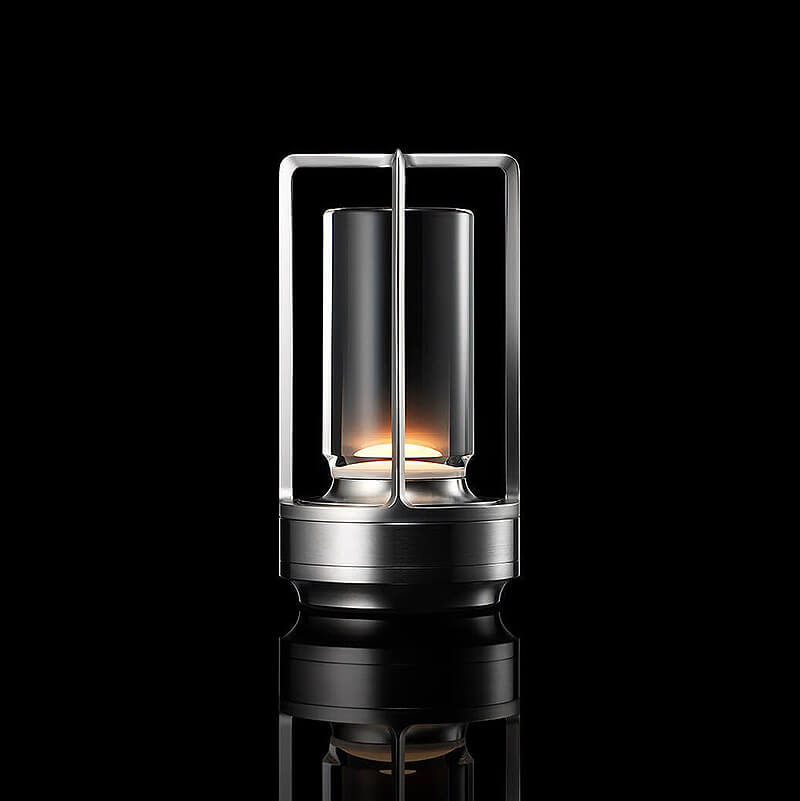 Silver-finish lamp with a glass cylinder inside an open metal frame, lit warmly against a black studio background. 10