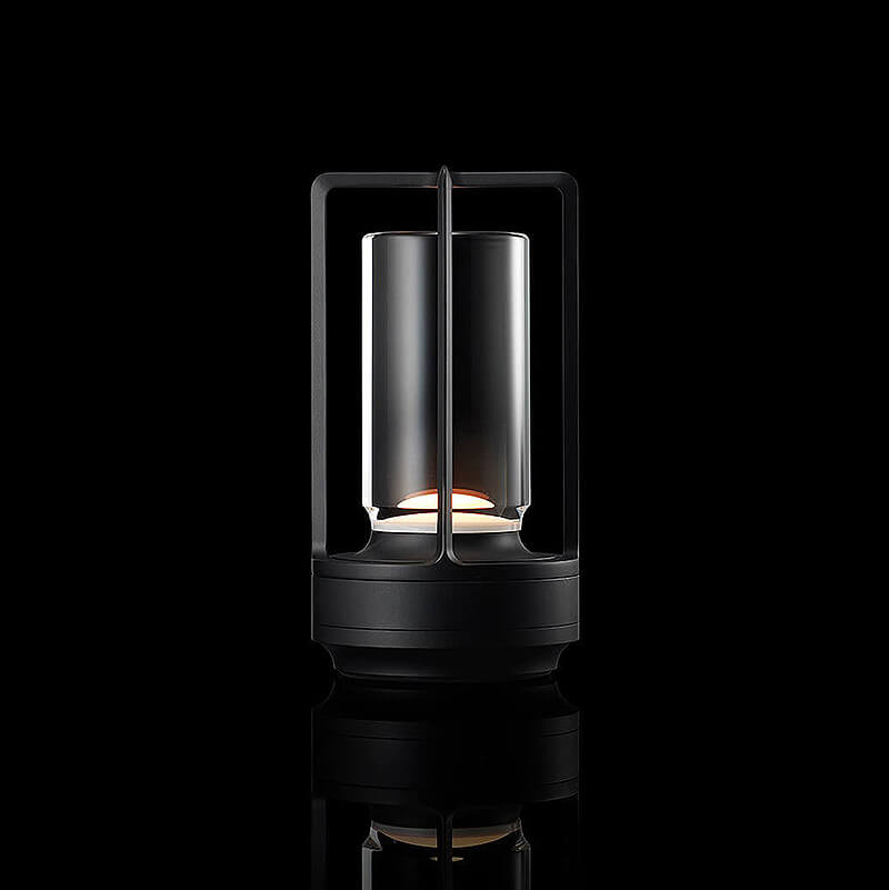 Black-finish lamp with a glass cylinder inside an open metal frame, glowing warmly against a black studio background. 11