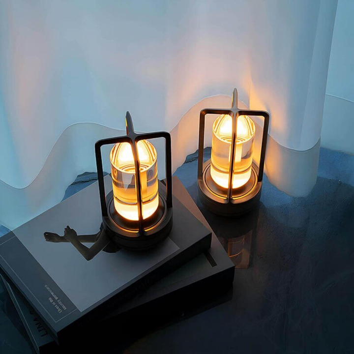 Two dark-framed lamps glowing amber on a stack of books beside a sheer white curtain. 3