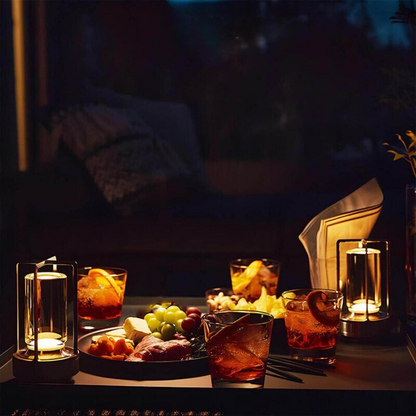 Two lit lamps on a dark table among cocktails, a grazing platter and a folded napkin for an evening gathering. 6