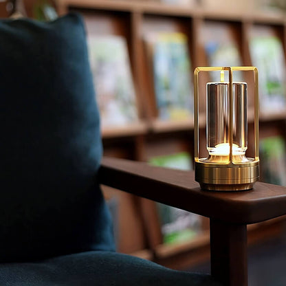 Gold-finish lamp lit on the wooden arm of a dark teal armchair, with bookshelves blurred behind. 8