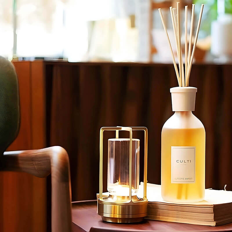 Gold-finish lamp glowing on a side table beside a reed diffuser bottle and a stack of books. 9