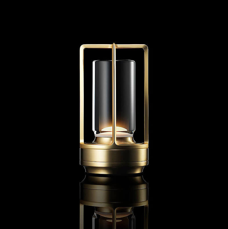 Gold-finish metal frame lamp with a clear glass cylinder, glowing softly against a black studio background with reflection. 1