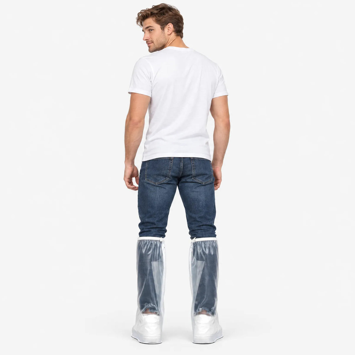 Back view of a man in a white t-shirt and jeans wearing clear overshoes over his trainers, looking over his shoulder. 4