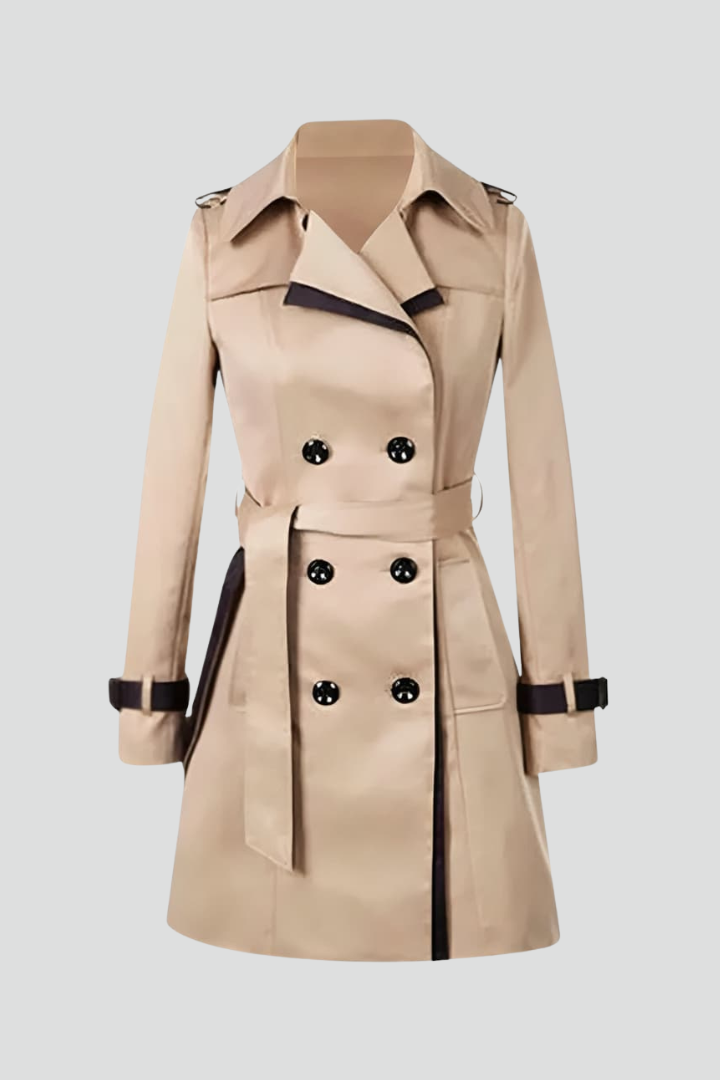 Beige double-breasted trench coat laid flat against a pale background, showing dark contrast trim, buttoned cuff straps and a tied belt. 1
