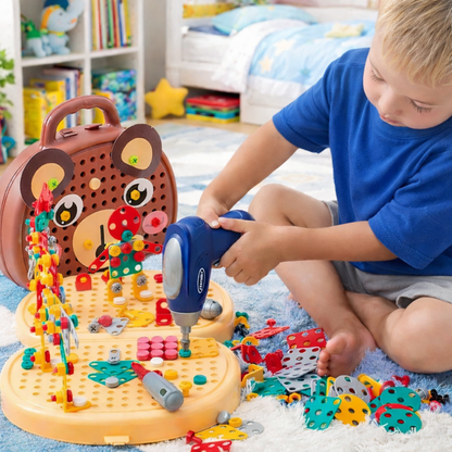 Young boy in a blue t-shirt sits on a rug using the toy drill on a building board beside the bear-faced carry case. 1