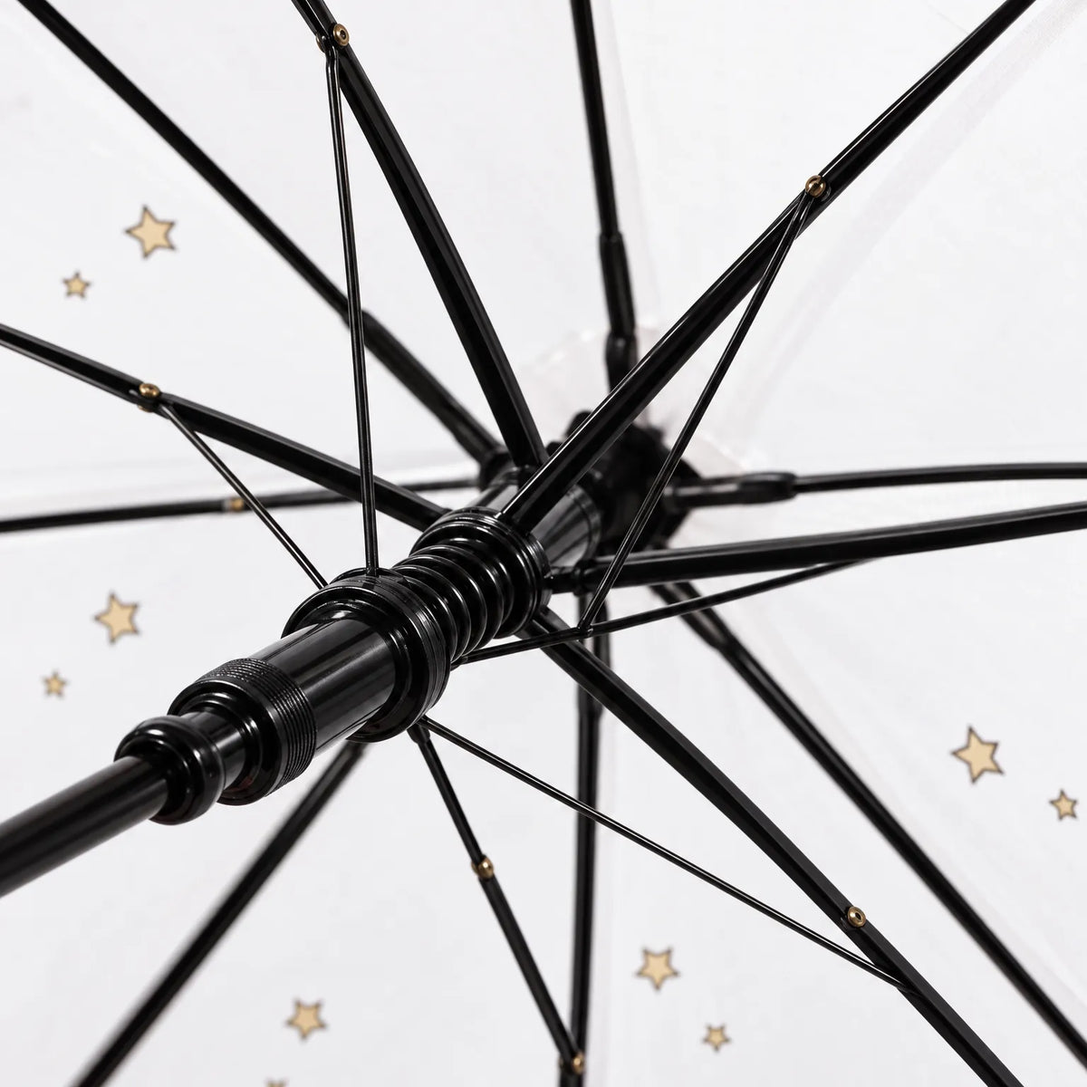 Close-up underneath the canopy showing the black ribs, spring runner and shaft, with small gold stars printed on the clear fabric. 6