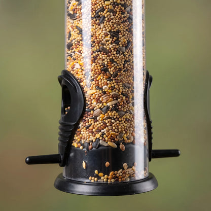 Close-up of the lower part of a seed-filled clear tube feeder, showing black feeding ports, perches and base tray. 3