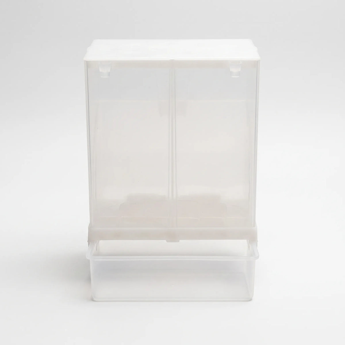 Front view of the clear plastic seed dispenser with a white lid and an attached catch tray at the bottom. 1