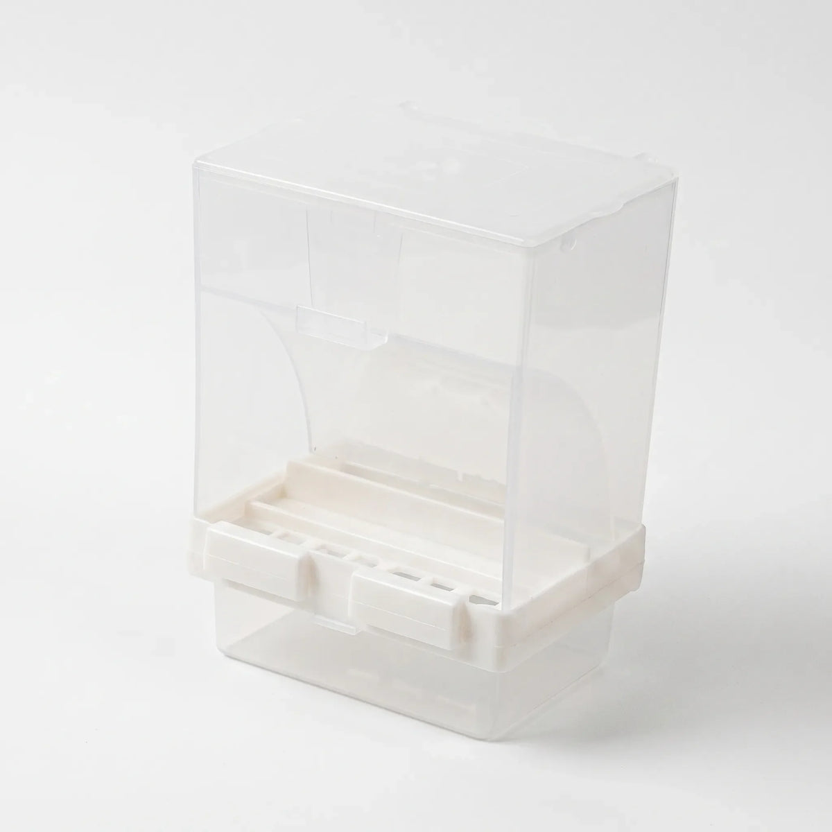Three-quarter view from the front of the empty dispenser, showing the curved opening, white feeding ledge with slots and the tray beneath. 4