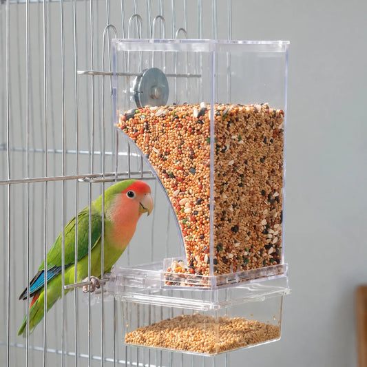 Green lovebird with a red face perched on the cage bars beside the seed-filled clear feeder, showing it in use. 2