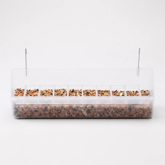 Long clear plastic cage feeder with two metal hanging hooks, filled with mixed seed and a row of small divided compartments along the front. 1
