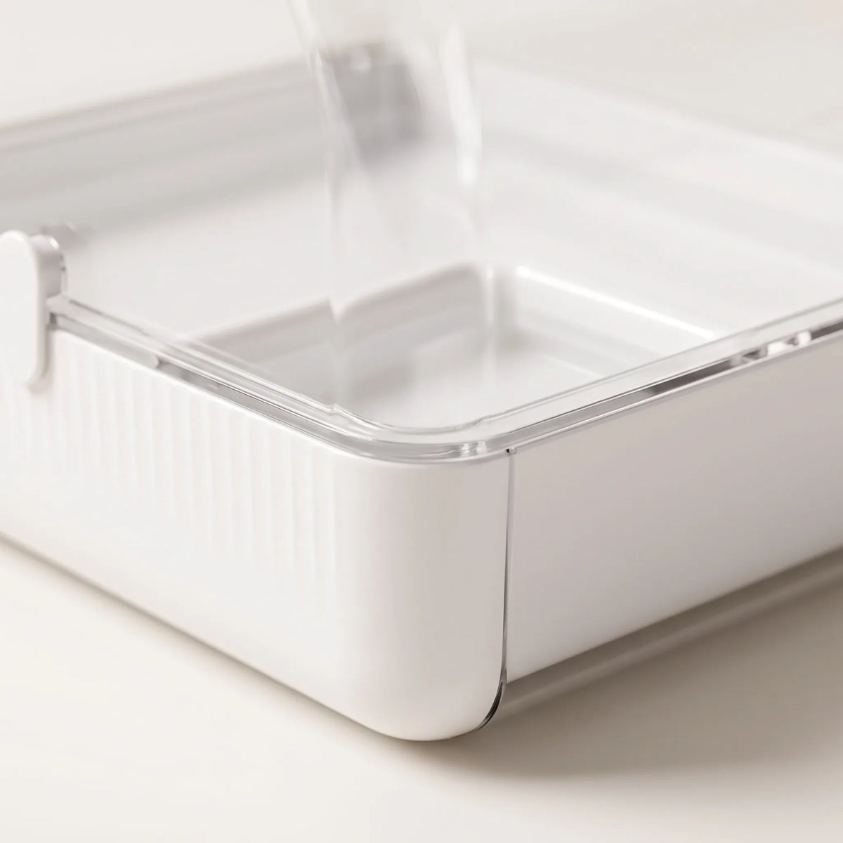 Close-up of the white ribbed tray corner with its clear rim and latch, showing the shallow water compartment inside. 3