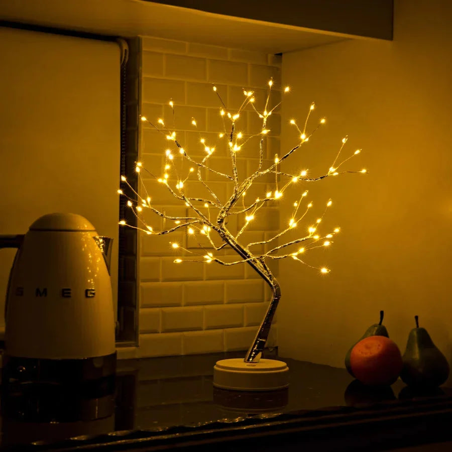 Tree lamp glowing on a kitchen worktop in front of white tiles, next to a kettle and fruit 5
