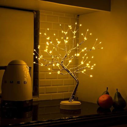 Tree lamp glowing on a kitchen worktop in front of white tiles, next to a kettle and fruit 5
