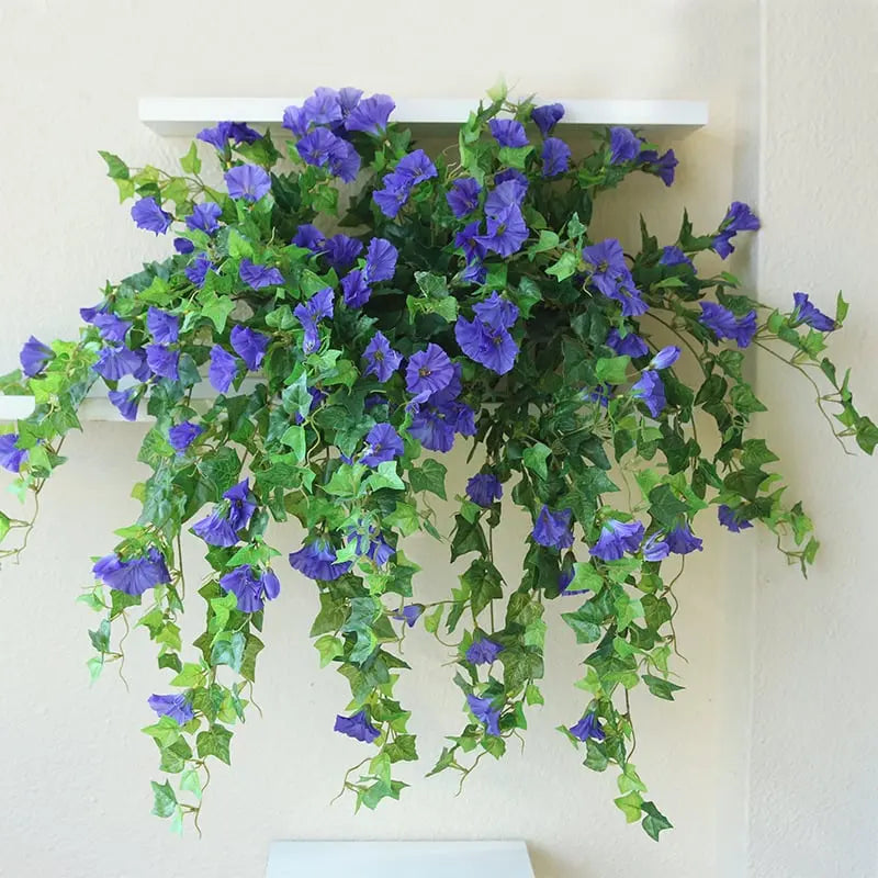 Blue-purple flowers and trailing green vines draped over a white wall shelf, hanging down against a cream wall. 4