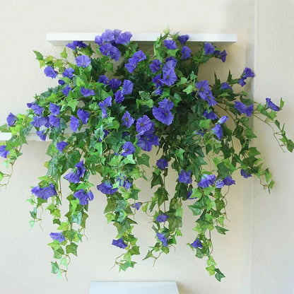Blue-purple flowers and trailing green vines draped over a white wall shelf, hanging down against a cream wall. 4
