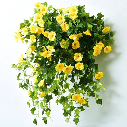 Yellow flowers and green leafy vines on a white wall, hanging in a loose cluster with a soft shadow behind. 5