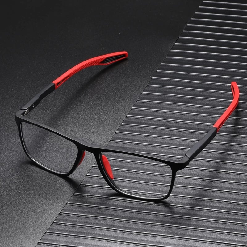 Black square-framed glasses with red arm tips and nose pads, resting on a dark ridged surface 2