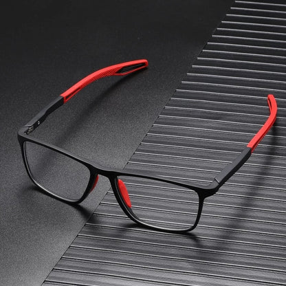 Black square-framed glasses with red arm tips and nose pads, resting on a dark ridged surface 2