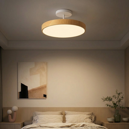 Light oak-effect round light with a white stem hanging over a neutral bedroom, above a bed with cream bedding and abstract wall art. 7