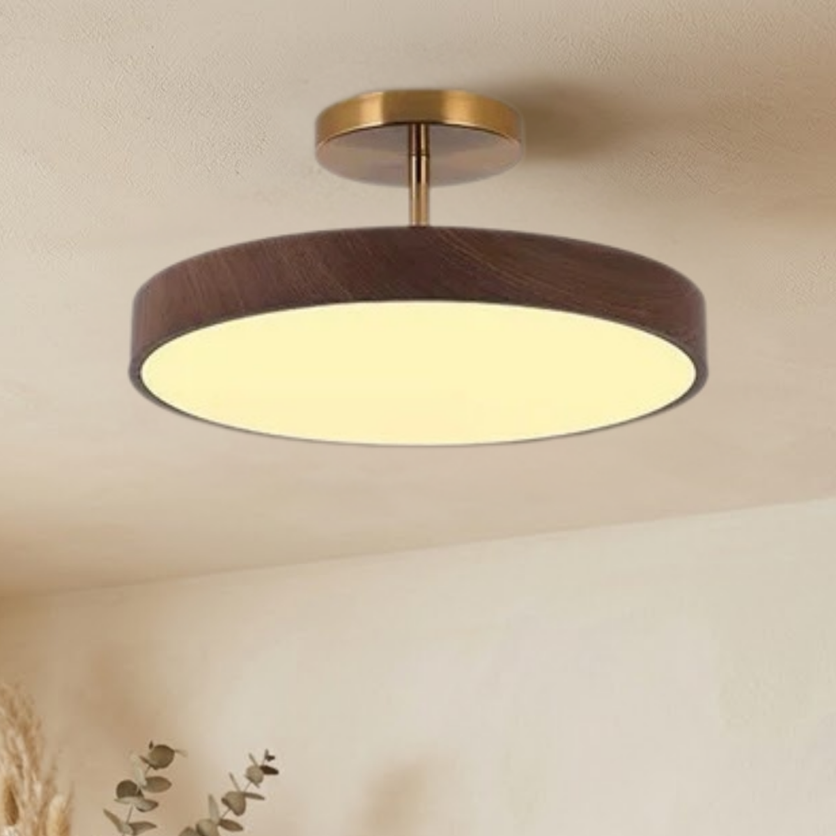 Dark wood-effect version lit and hanging from a cream ceiling, with eucalyptus sprigs and dried grasses below, showing a slightly warmer glow. 3