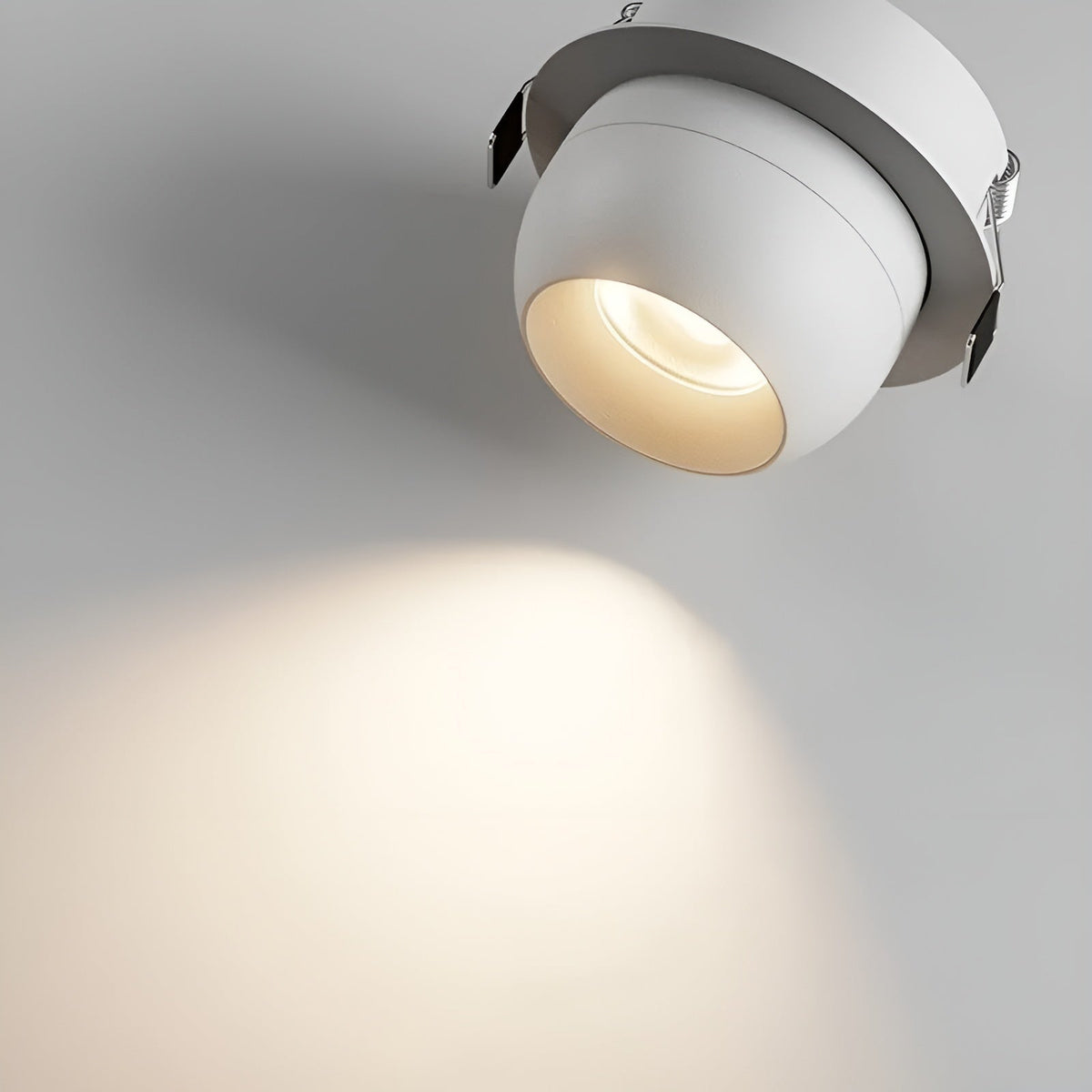 Close-up of a white recessed spotlight showing its rounded head, metal mounting clips and warm light beam 4