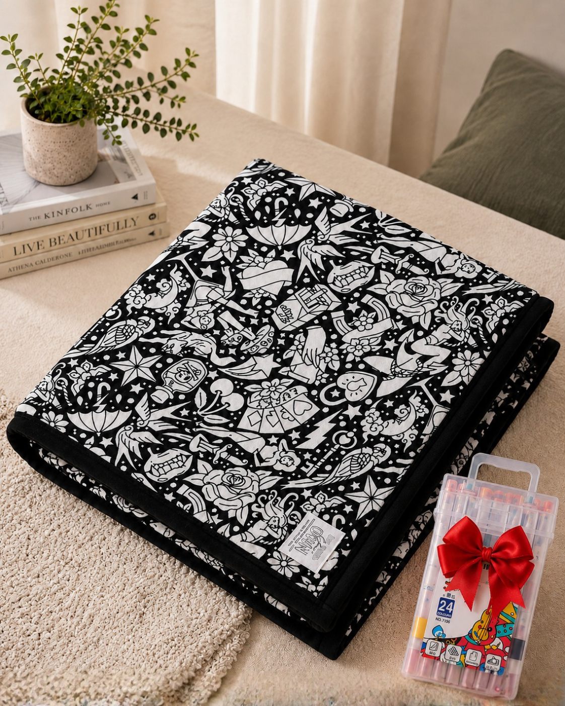 Folded blanket with a black and white tattoo-style design of roses, hearts, swallows and stars beside a marker set 8