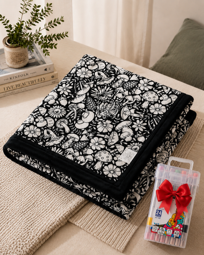 Folded black blanket printed with white mushroom and daisy outlines, with a black border and a bowed box of pens 9