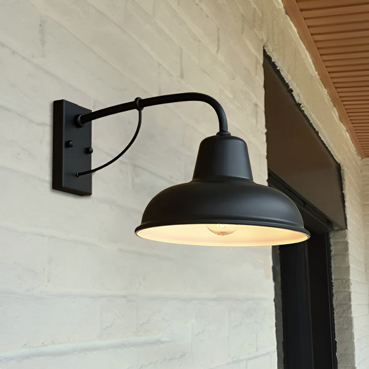 Black curved-arm wall light lit on a whitewashed brick wall, with the bulb glowing under the pale-lined shade. 5