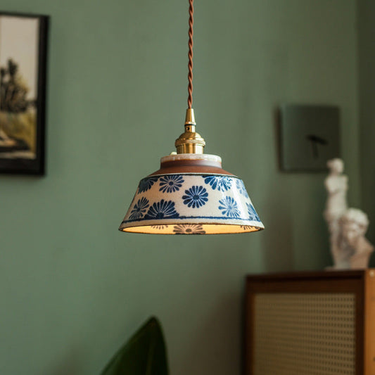 Pendant with blue daisy-patterned ceramic shade and brass fitting hanging on a twisted brown cord against a sage green wall. 1