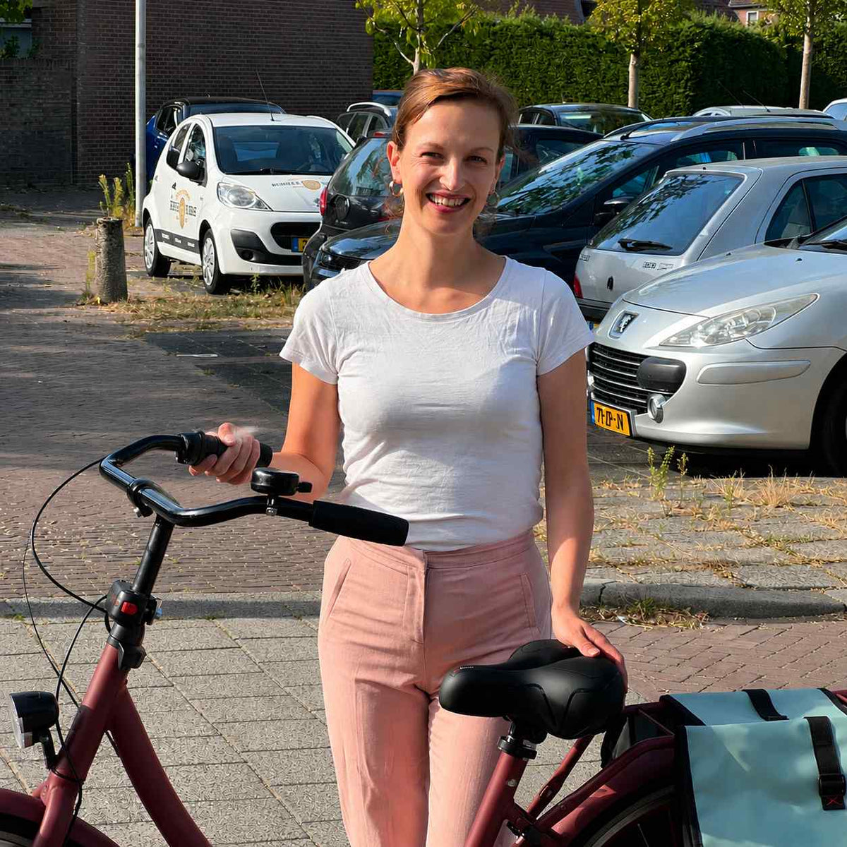 Woman in pink trousers standing beside a dark red city bike, resting a hand on its black saddle. 7