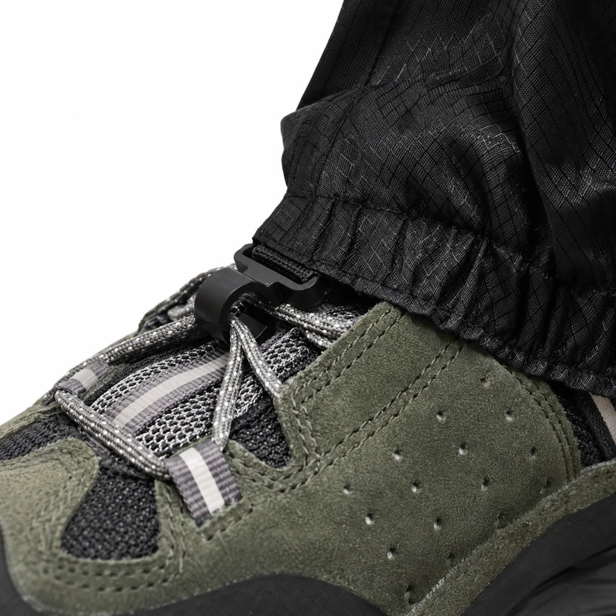 Close-up of the black gaiter hem clipped to the boot laces with a small plastic hook, showing the ripstop fabric texture. 6